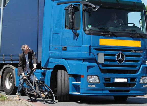 Ein rechtsabbiegender LKW mit einem Radfahrer, der fast mit ihm kollidiert. 
