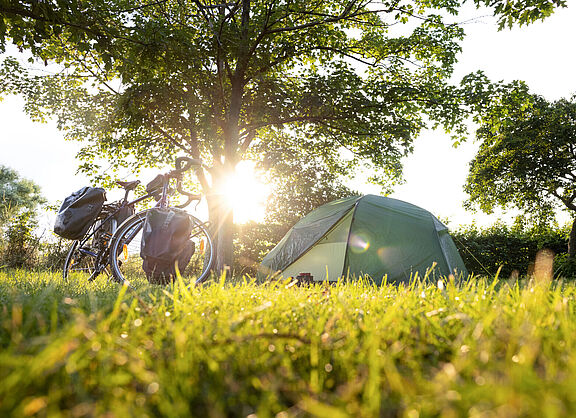 Fahrrad mit Packtaschen und Zelt bei Sonnenuntergang.