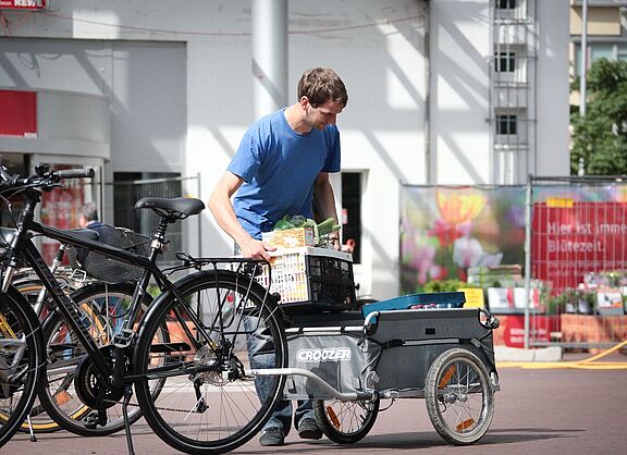 Ein Mann belädt einen Fahrradanhänger vorm Supermarkt. 