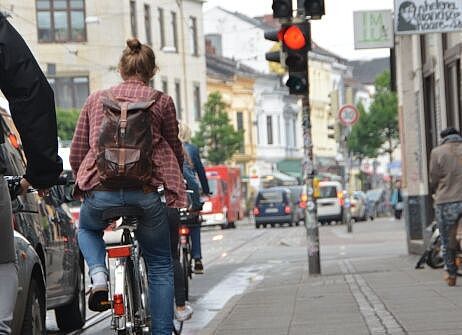 Radfahrende fahren auf schmelaem Bürgersteigradweg neben parkenden Autos. 