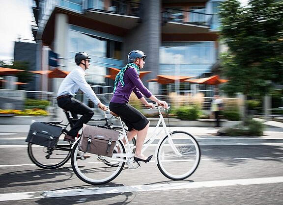 Zwei Menschen fahren nebeneinander Fahrrad in einem städtischen Umfeld.