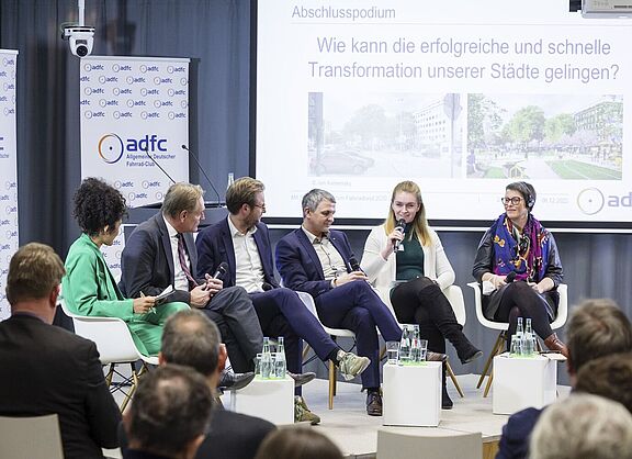 Bild von einem Podium mit den Teilnehmenden einer Podiumsdiskussion. 