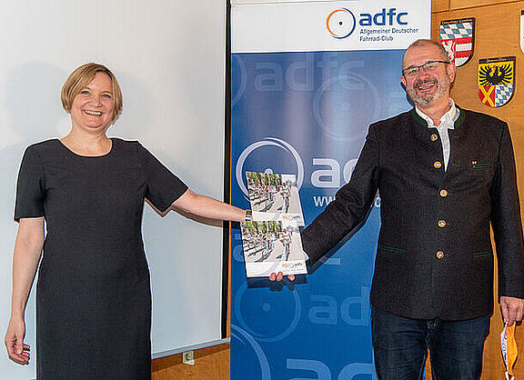 Bernadette Felsch und Armin Falkenhein präsentieren vor blauem Hintergrund die Broschüre "30 Jahre ADFC Bayern". 